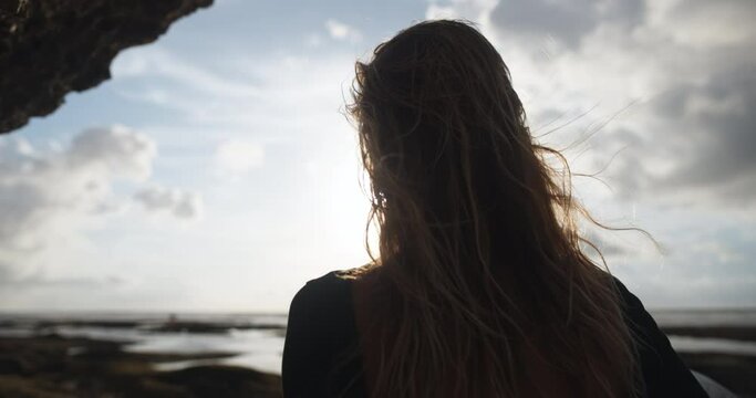 Back view attractive Caucasian female surfer in rays of bright sun going straight to sea to ride waves on surfboard. Rear view of sporty fit healthy female athlete surfer with surfboard on beach.