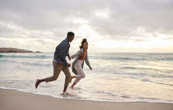 Young multiethnic couple running through the surf on a beach
