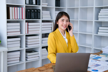 Young accountant business asian woman with smartphone to call marketing consultants and using laptop computer to analyze sales growth in the global workplace market. accounting concept.