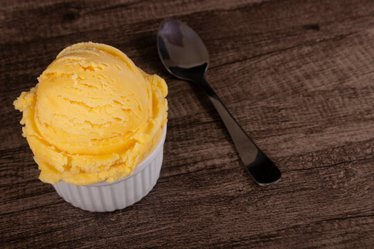 Vanilla ice cream served in a white bowl next to a spoon. Gourmet photograph of frozen desserts with empty space to the right of the image.