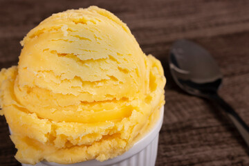 Vanilla ice cream served in a white bowl next to a spoon. Food aligned left background blurred .