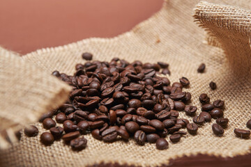 Roasted coffee beans on the rural rough sackcloth and the bright solid fond plain brown background