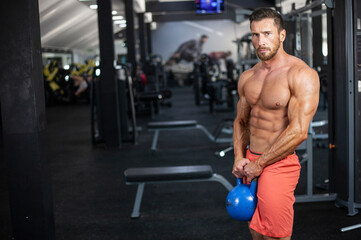 Fototapeta na wymiar Strong , powerful, muscular man holding blue kettlebell with both hands in a gym
