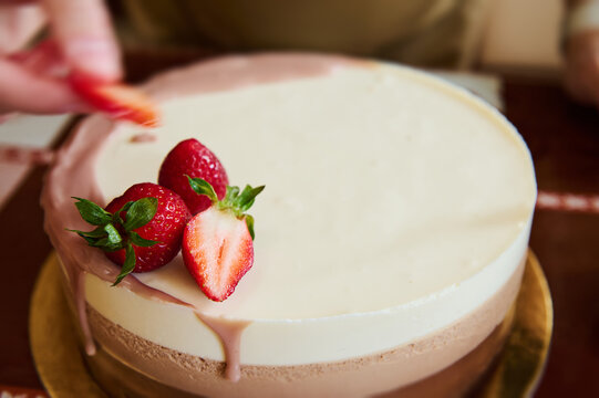 Selective focus pastry chef decorating a triple chocolate mousse cake with fresh strawberries. Confectionery. Copy advertising space. Sweet dessert with layers of white, milk and dark chocolate mousse