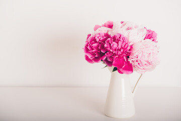 Beautiful bunch of fresh peonies in full bloom in vase against white background. Copy space for text. Minimalist floral still life with blooming flowers.