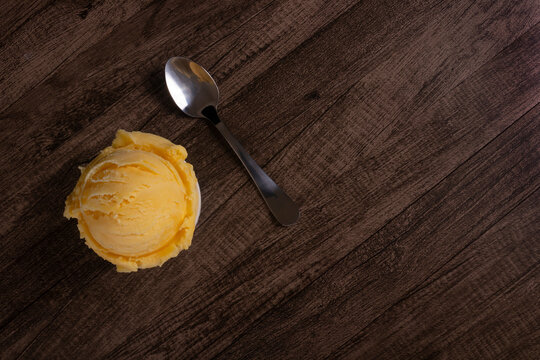 Tasty yellow cream ice cream served in a white bowl next to a spoon. Top photography with elements aligned on the left and empty space on the right. Ice cream ball.