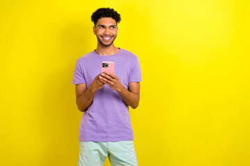 Portrait of handsome cheerful guy hold smart phone beaming smile look empty space isolated on yellow color background