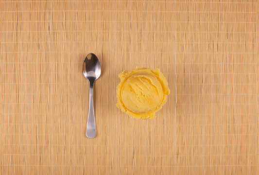 Tasty yellow ice cream served in a white bowl with a spoon on the side and a wooden background. Top view gourmet gelato photography.