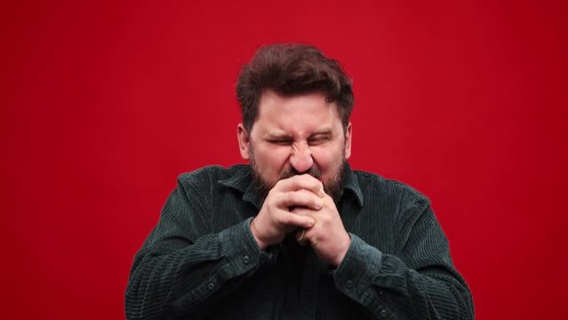 Bearded man emotionally eating red hot chilli pepper against red studio background. Spicy taste, burning mouth. Concept of food, vegetables, taste, grocery, human emotions. Ad