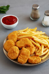 Homemade Chicken Nuggets and French Fries with Ketchup on gray background, side view.