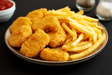 Homemade Chicken Nuggets and French Fries with Ketchup on black background, side view. Close-up.