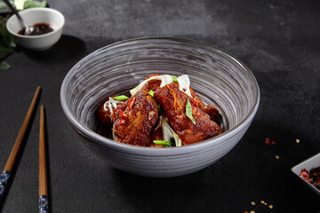 Fried Buffalo wings in Asian style on a black background. Sliced greens on wings, spices, and chopsticks in the background