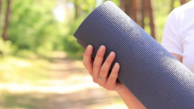 Active girl holding a fitness mat, sports equipment. Sports outdoors in the forest. The girl starts her workout outside. Girl with a mat for fitness and yoga in her hands, close-up