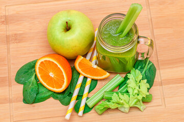 Fresh Green Smoothie of Apple, Celery, Spinach and Orange in Glass Smoothie Jar with Yellow Cocktail Straw on Wooden Cutting Board. Vegan Detox Drink. Vegetarian Culture. Healthy Eating and Fruit Diet