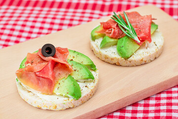 Rice Cake Sandwich with Avocado, Jamon, Olives and Rosemary on Wooden Cutting Board. Easy Breakfast. Quick and Healthy Sandwiches. Crispbread with Tasty Filling. Healthy Dietary Snack
