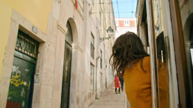 Beautiful and authentic millennial young woman lean out of window of old tram in Lisbon, Portugal city centre. Concept amazing european summer vacation, wanderlust trip in cinematic urban destination