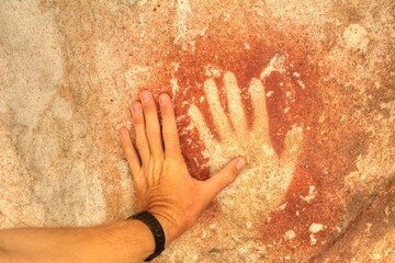 Photo of a hand touching a rock with a hand print in Cueva de las Manos, Argentina