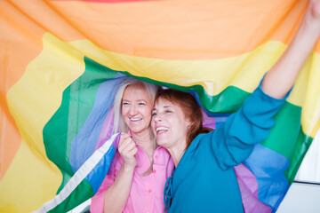 Lgtbi senior couple smiling while embracing each other with an lgtbi flag. Concept: pride, lgtbi...