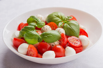 A plate of caprese salad on a table with a white linen tablecloth. Mediterranean cuisine. Focusing on the basil leaves on top. Macro with shallow dof.