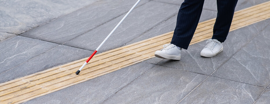 Close-up of the legs of a blind businesswoman walking along a tactile tile with a cane. Widescreen. 
