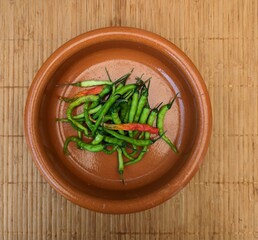 Mexican green and red chiles de arbol inside traditional clay plate, rattan background