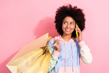 Photo of funny beautiful small schoolgirl hold boutique bags speak communicate telephone isolated on pink color background