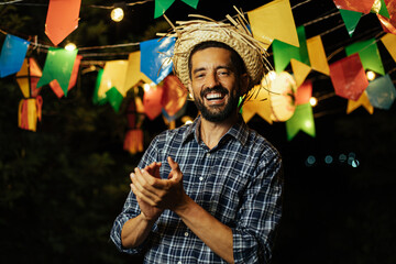 A lively man in a straw hat and vibrant attire, dancing with enthusiasm amidst the joyful Brazilian June festival - Festa Junina