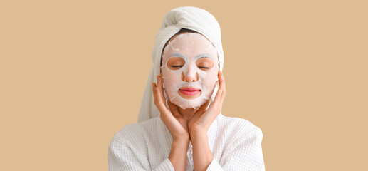 Young woman with applied sheet facial mask on beige background