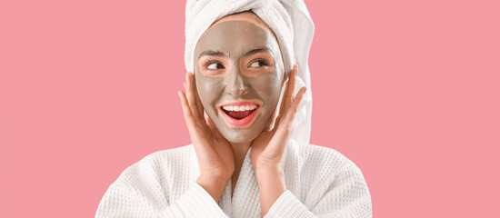 Happy young woman with applied clay mask on pink background