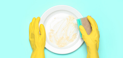 Hands in rubber gloves and with sponge washing dirty plate on turquoise background