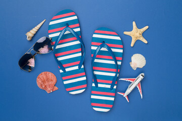 Flip flops with sunglasses and airplane on color background, top view