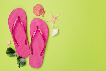 Flip flops with sunglasses and airplane on color background, top view