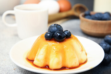 Plate with delicious pudding and blueberries covered by caramel syrup on grunge background