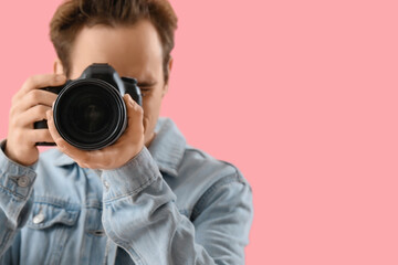 Young male photographer with modern camera on pink background