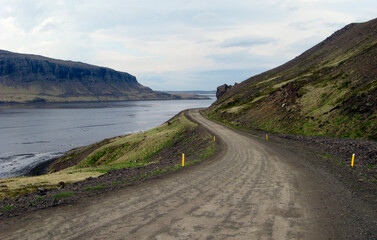 A road winds alongside a mountain and river in Iceland.