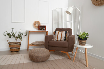 Cozy brown armchair with cushion, coffee table and wicker pouf in living room