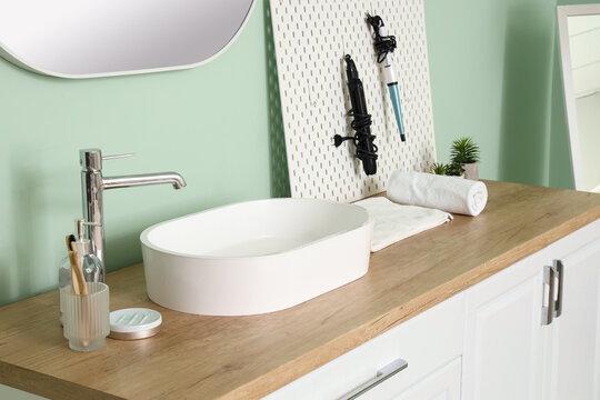 Counter With Sink Bowl, Tooth Brushes And Hair Styling Tools On Pegboard In Bathroom