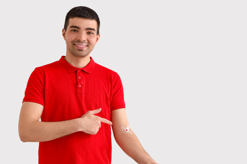 Young blood donor pointing at applied medical patches on light background