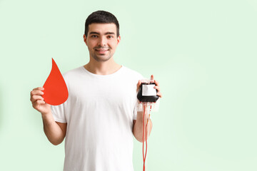 Young donor with blood pack and paper drop on green background