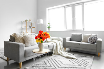 Interior of light living room with cozy sofas and tulip flowers on coffee table