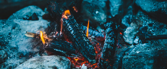 Fototapeta na wymiar Vivid smoldered firewoods burned in fire close-up. Atmospheric warm background with orange flame of campfire. Unimaginable full frame image of bonfire. Burning logs in beautiful fire. Wonderful flame.