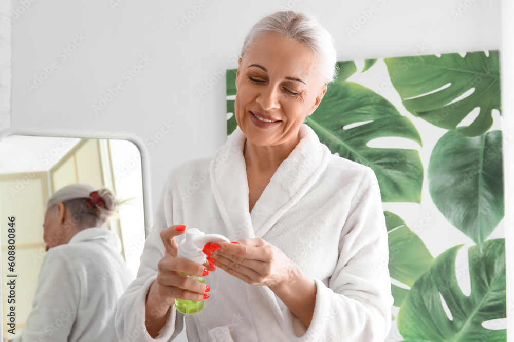 Sticker mature woman applying cosmetic product with cotton pad in bathroom