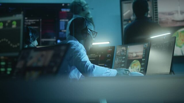 Diverse flight control employees in headsets monitor space mission on computers in mission control center. Team clap hands after successful space rocket launch displayed on big digital screens.