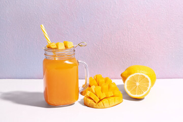 Mason jar of fresh mango smoothie and lemon on purple background