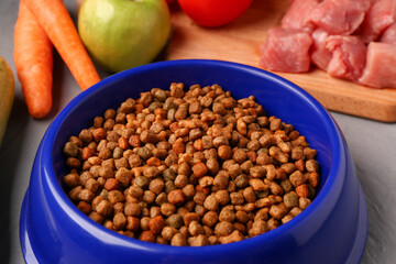Bowl with dry pet food, raw meat and natural products on color wooden background, closeup