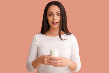 Surprised young woman with glass of milk on beige background