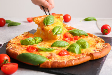 Female hand taking slice of tasty pizza margarita on white table, closeup
