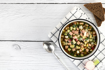 Okroshka - russian cold soup with vegetables, sausage, herbs, kvass and black bread on a white background. Copy space.