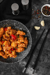 Tasty sweet and sour chicken in bowl with spices on grey background