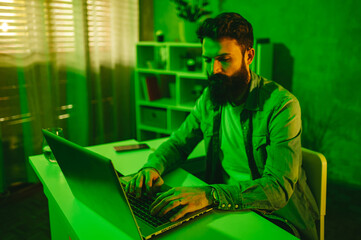 An IT expert is developing new software while sitting in neon green-lighted home office.